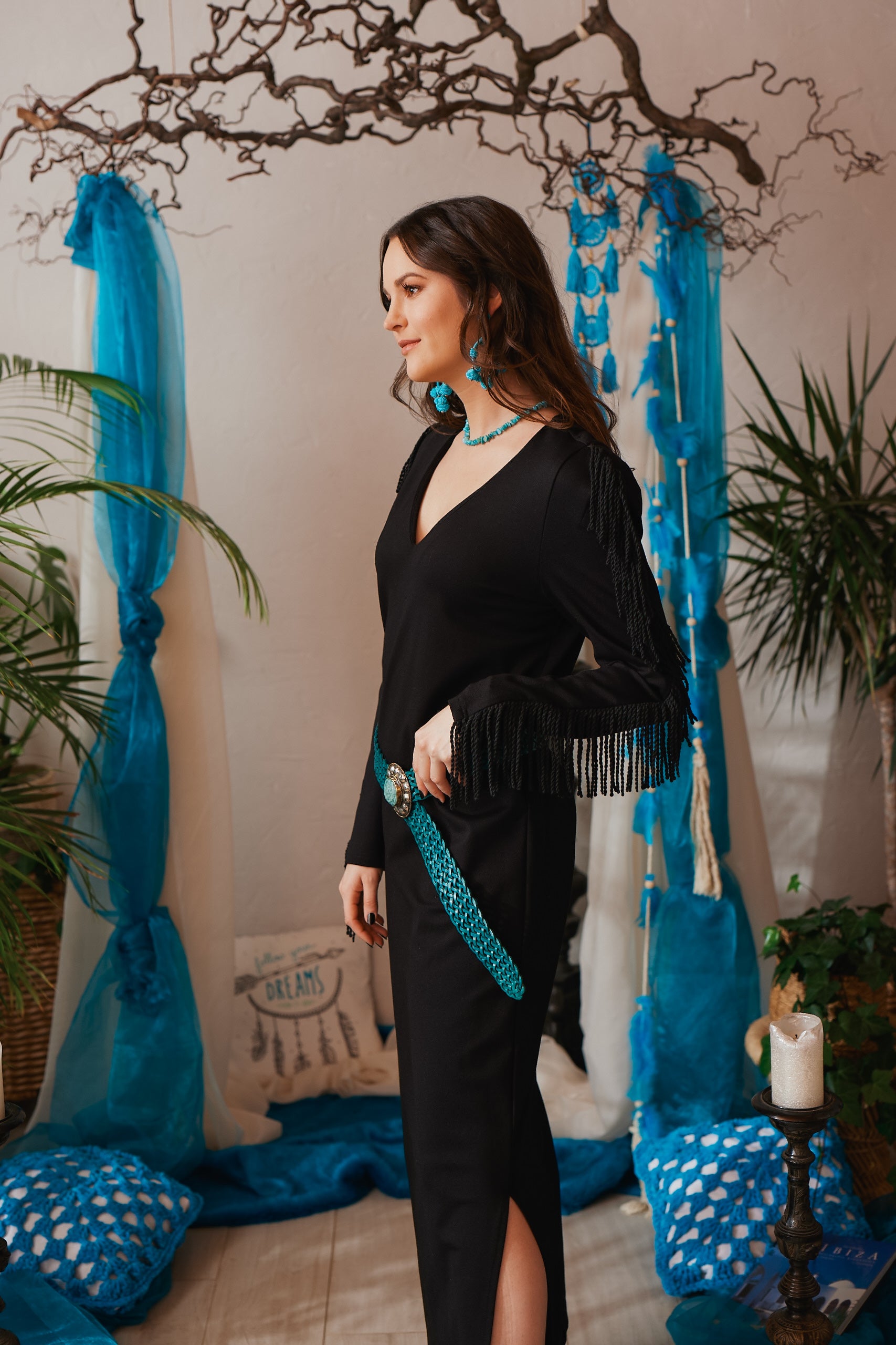Dieses lange, schwarze Boho-Stretchkleid überzeugt mit gedrehten Fransen an den Ärmeln und einem eleganten V-Ausschnitt. Schulterpolster und seitliche Schlitze verleihen dem Kleid eine moderne Silhouette. Das blickdichte, formbeständige Stretchmaterial sorgt für hohen Tragekomfort und eine entspannte Passform. Vielseitig kombinierbar, lässt es sich mit einem Gürtel individuell stylen – ideal für einen lässigen Bohemian Look. Das streng limitierte Design macht es zu einem besonderen Highlight
