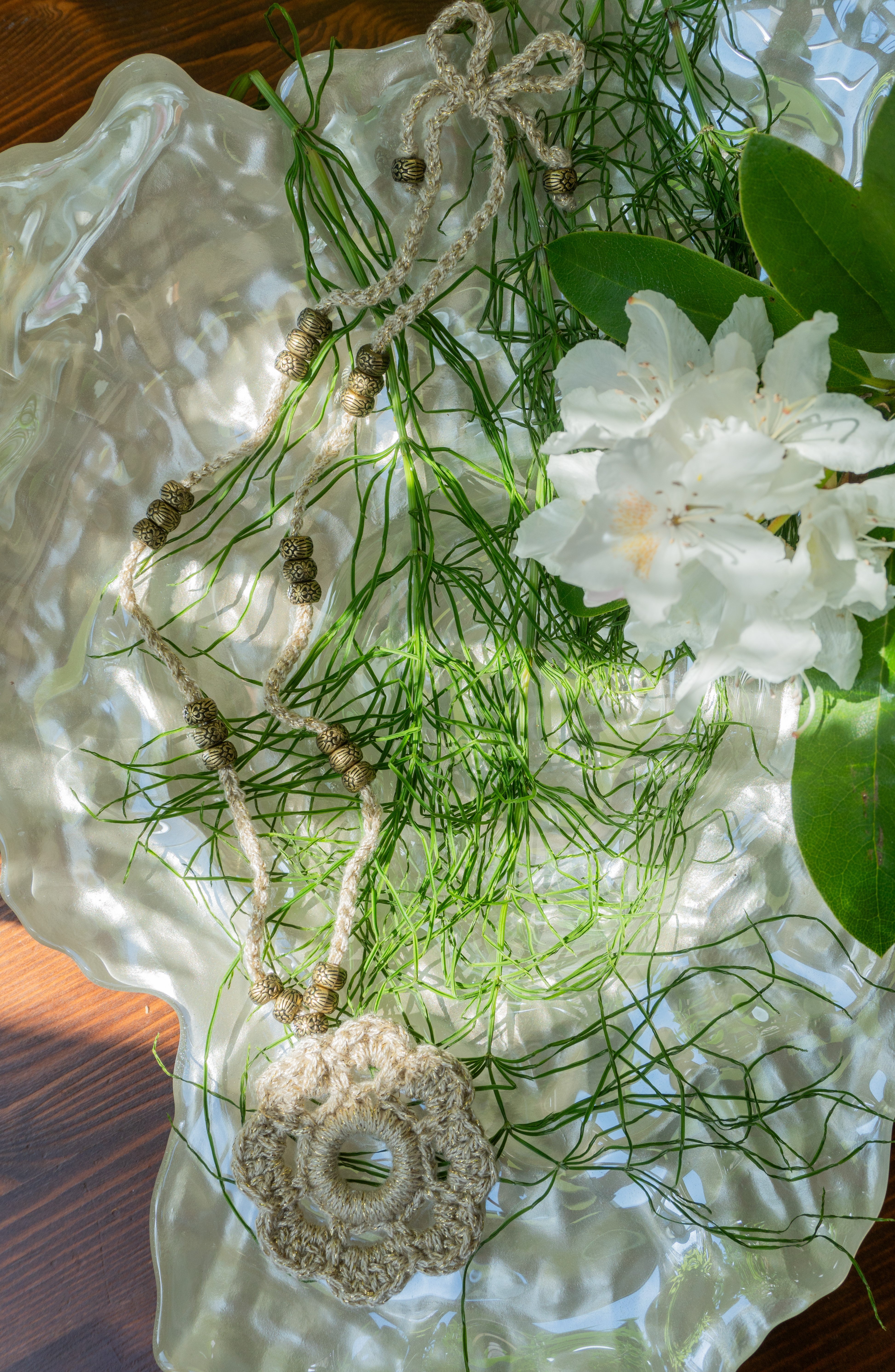 Verleihe deinem Boho Look einen Hauch von Eleganz mit unserer handgefertigten Häkelkette. Das Unikat besteht aus edlem metallic-gold Effektgarn und ist mit einem Häkel-Blumen Anhänger sowie passenden Ethno Style Perlen versehen. Perfekt als sommerliches Accessoire.